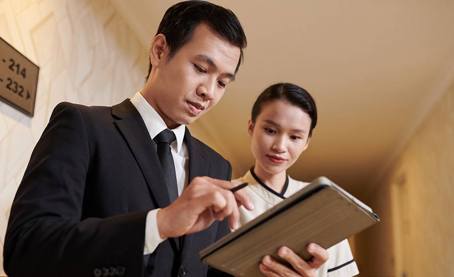 A hotel manager with a tablet checking employee schedules together with an employee​