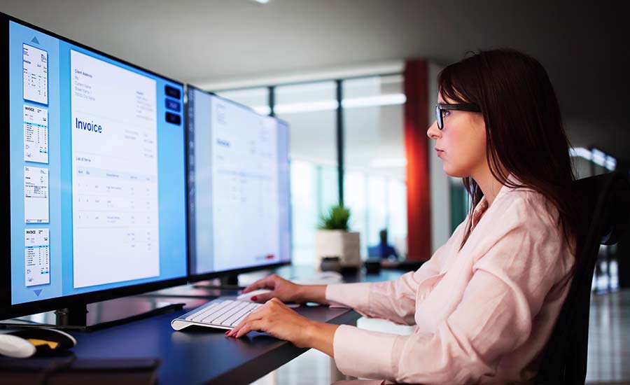 A woman looking at invoices on a big monitor​